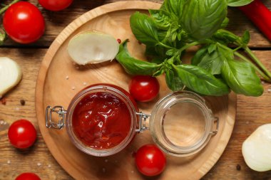 Lezzetli ketçap kavanozu ve ahşap arka planda farklı malzemeler.