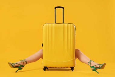 Yüksek topuklu ve sarı arka planda bavullu genç bir kadın oturuyor.