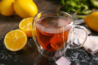 Bir fincan sıcak içecek, çay poşetleri ve arka planda limonlar.
