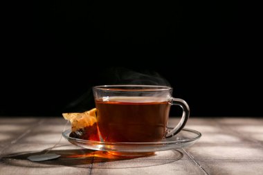 Bir fincan sıcak içecek. Koyu renkli duvara karşı gri fayansların üzerinde çay poşeti var.