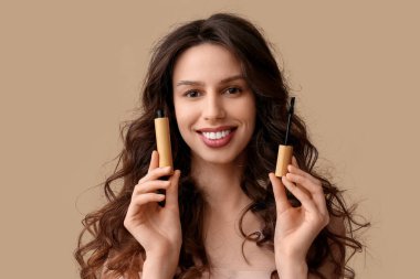 Beautiful young woman with mascara on brown background