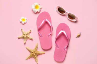 Güneş gözlüklü, yıldız balıklı ve pembe arka planda çiçekli şık parmak arası terlikler.