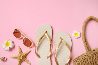 Güneş gözlüklü bej terlikler, denizyıldızı, hasır çanta ve pembe arka planda çiçekler.