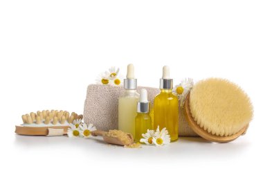 Masaj vücut fırçaları, kozmetik ürünleri şişeleri ve beyaz arka planda izole edilmiş papatya çiçekleri, yakın plan