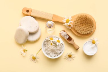 Bej arka planda papatya çiçekleri, spa taşları, kâseler ve bir şişe kozmetik ürünleri içeren kompozisyon, yakın plan