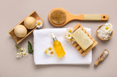 Masaj vücut fırçası, kozmetik ürün şişesi ve gri arka planda papatya çiçeği kompozisyonu, yakın plan.