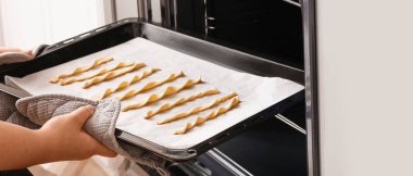 Bir kadın çiğ İtalyan Grissini ile pişirme tepsisini fırına koyuyor.