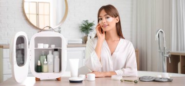 Küçük buzdolabı ve kozmetik ürünleriyle banyoda güzel bir genç kadın.