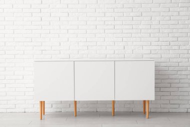 Odanın hafif tuğlalı duvarının yanındaki beyaz çekmeceler.