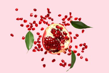 Tohumları ve yaprakları pembe arkaplanda uçuşan taze nar.