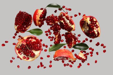 Tohumları ve yaprakları gri arkaplanda uçuşan taze narlar.