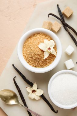 Aromatik vanilya şekerli kaseler, çiçekler ve bej arka planda çubuklar