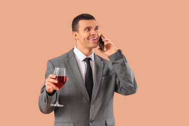 Bir bardak şarapla bej arka planda telefonla konuşan genç bir işadamı.