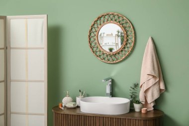 Tezgahta banyo malzemeleri ve banyoda yeşil duvarın yanında şık bir ayna olan modern lavabo.