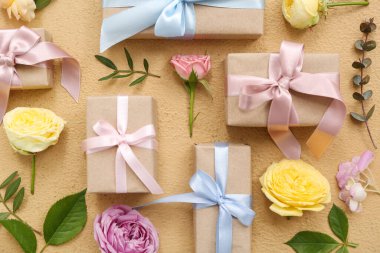 Paketli kağıt hediye kutuları ve bej arka planda güzel çiçekler olan kompozisyon