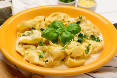 Beyaz ahşap arka planda soslu ve fesleğenli bir kase haşlanmış hamur köftesi.