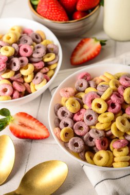 Renkli tatlı mısır gevreği halkaları ve beyaz fayans masasında çilekler.