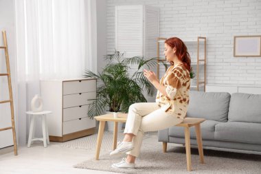 Evde cep telefonu kullanan genç bir kadın.