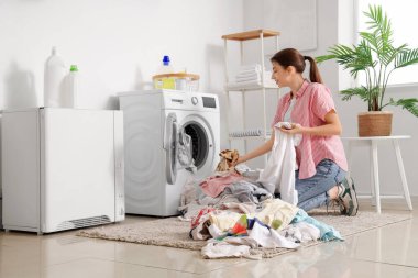 Kirli çamaşırları evdeki çamaşır makinesine koyan genç bir kadın.