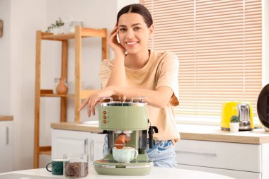 Mutfakta modern kahve makinesi olan güzel, genç ve mutlu bir kadın.