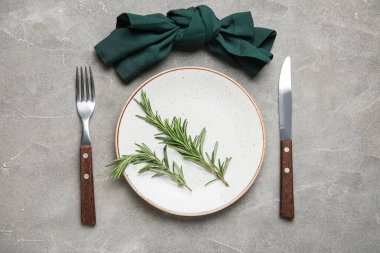 Gri grunge arka planda peçete, çatal bıçak ve biberiye ile şık masa ayarları