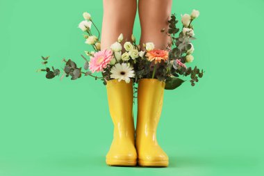 Woman with flowers in gumboots on green background, closeup