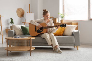 Oturma odasındaki kanepede gitar çalan genç kadın.