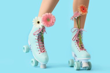 Paten giymiş kadın bacakları ve mavi arka planda Gerbera çiçekleri.