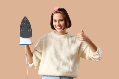 Demiri olan gülümseyen genç bir kadın bej arka planda baş parmağını kaldırıyor.