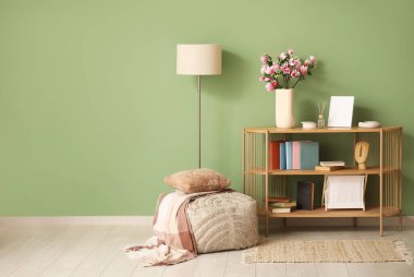 Pouf, vazoda yeşil duvarın yanında çiçek açan manolya dalları ve dekorasyonu olan raf ünitesi.