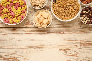 Kahverengi ahşap arka planda farklı lezzetli mısır gevrekleri olan kaseler.