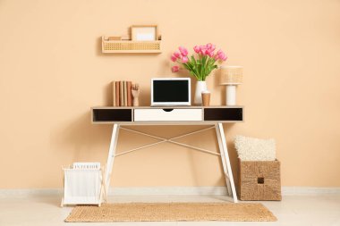 Modern dizüstü bilgisayar, kitaplar ve bej duvarın yanında güzel lale çiçekleri olan şık bir çalışma alanı.