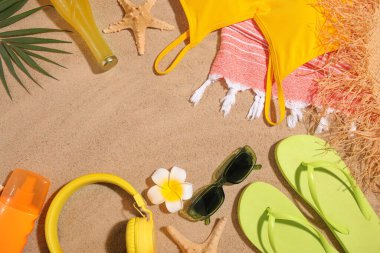 Şık plaj aksesuarları, bir şişe içki ve kumdaki kulaklıklar.