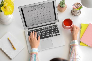 Masasında takvim ve çay fincanı olan dizüstü bilgisayarı olan bir kadın.