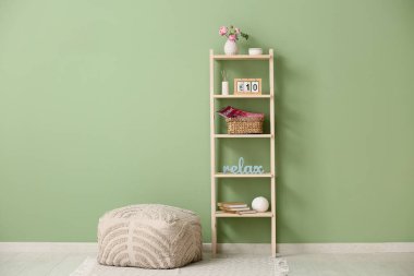 Takvim, dekor, dergiler ve renk duvarının yanında puf bulunan ahşap raf.