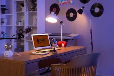 Podcaster 'ın iş yeri. Karanlık stüdyoda dizüstü bilgisayarı, mikrofonları ve parlak lambaları var.