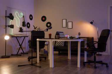 Karanlık podcaster stüdyosunun içinde iş yeri, vinil diskler ve parlayan lambalar var.