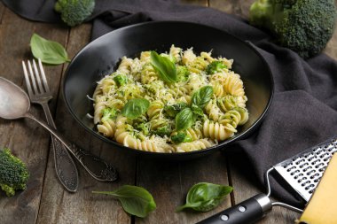 Bir kase lezzetli fusilli makarna brokoli ve ahşap zemin üzerinde fesleğen yaprakları.