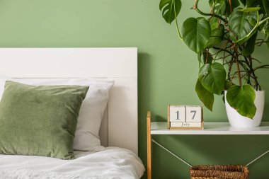 Küp takvimi. Yatak odasındaki yeşil duvarın yanındaki rafta bir palmiye ağacı var.