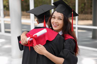 Mezuniyet gününde kucaklaşan diplomalı iki öğrenci.