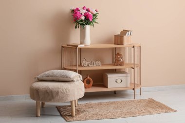 Pouf, raflama ünitesi ve vazo içinde güzel şakayık çiçekleri olan oturma odası.