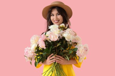 Pembe arka planda şakayık çiçekleri olan şapkalı genç bir kadın.