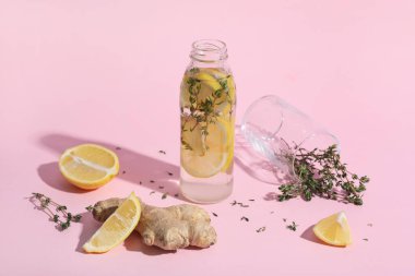 Pembe arka planda zencefil ve kekik ile doldurulmuş bir şişe taze limon.