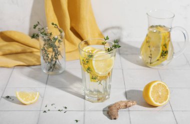 Bir bardak taze limon, zencefil ve kekik karıştırılmış beyaz fayans masasında.