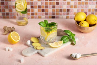 Açık pembe masada zencefil ve fesleğen yapraklı taze limonlu su.