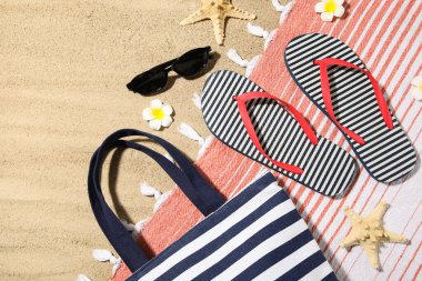 Arka plan olarak kumsalda plaj ayakkabıları ve plaj aksesuarları olan kompozisyon, yakın plan