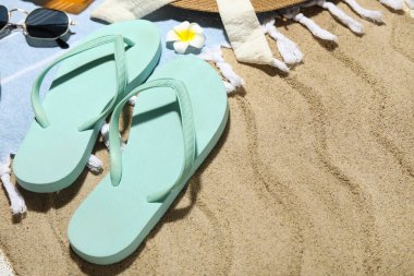 Arka plan olarak kumsalda plaj ayakkabıları ve plaj aksesuarları olan kompozisyon, yakın plan