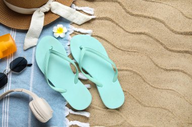 Plaj ayakkabıları, kulaklıkları ve kumsaldaki aksesuarları arka plan olarak, yakın plan.