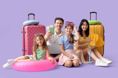 Diz üstü bilgisayarı ve bavulu olan turist ailesi leylak arka planda oturuyor.