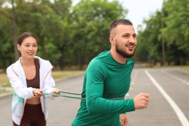 Sportif bir adam ve antrenör açık havada bantla egzersiz yapıyor.